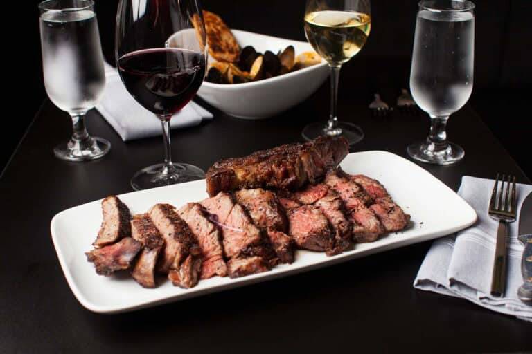 Sliced steak with wine and water on table