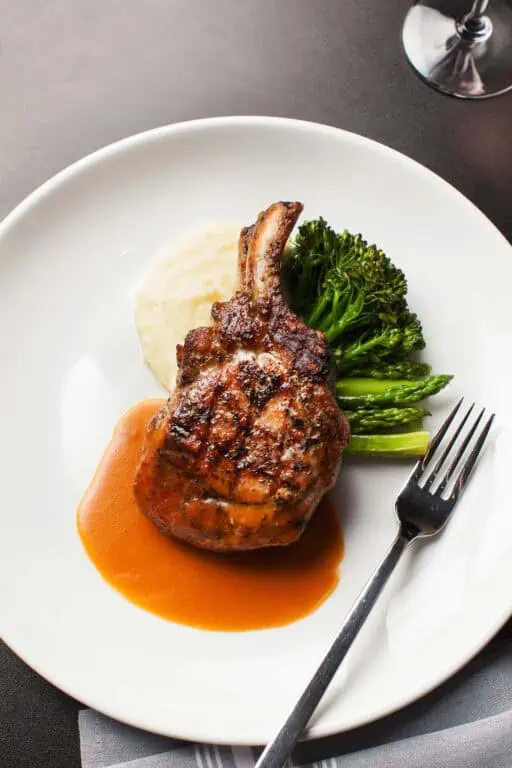 Grilled pork chop with vegetables and sauce on plate.