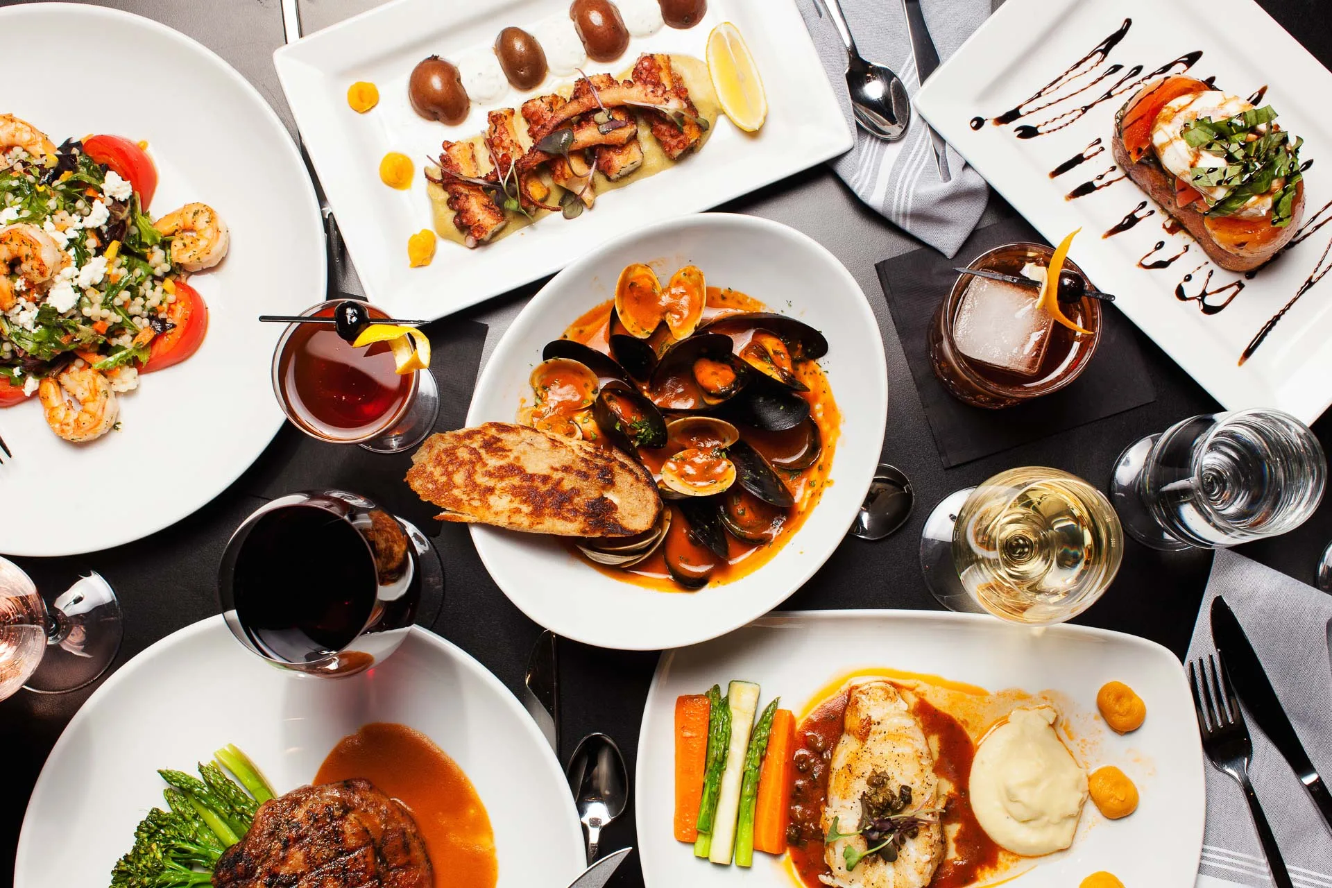 Gourmet meal with seafood, steak, and drinks.